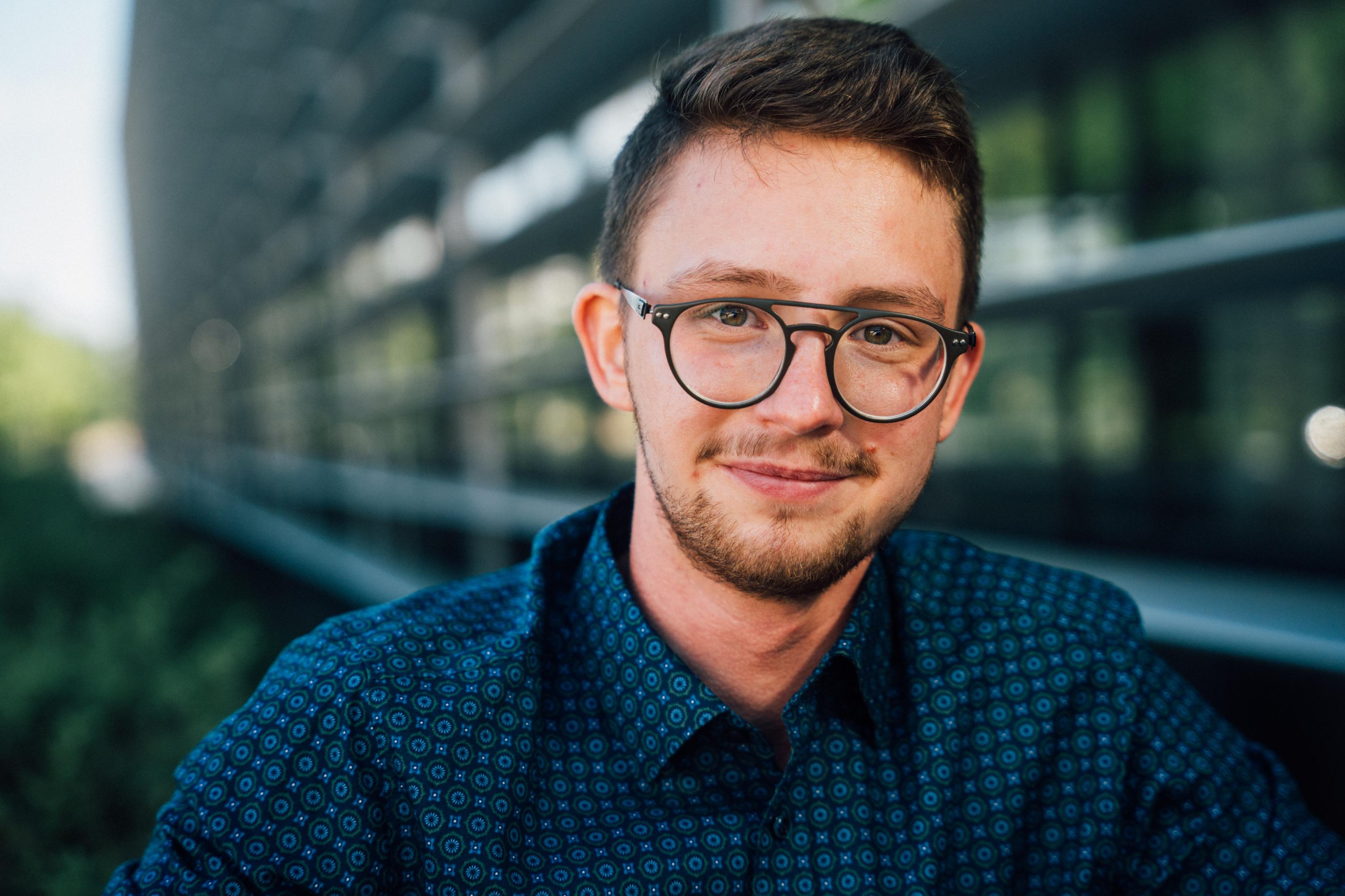 Vor einer Glasfassade stehend, schaut Luis Schäfer freundlich in die Kamera.